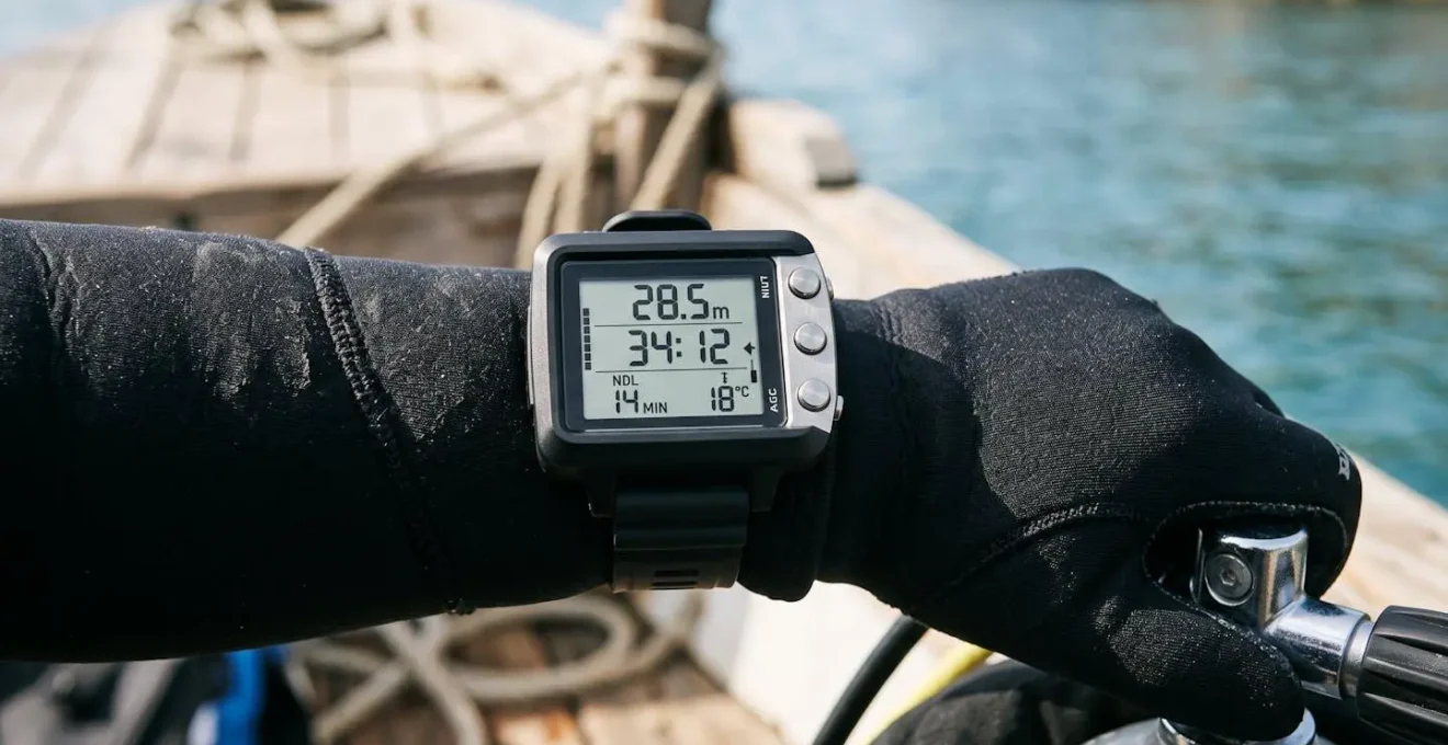 Gros plan sur ordinateur de plongée moderne au poignet d'un plongeur équipé, écran LCD affichant profondeur et temps de plongée, main gantée sur détendeur, fond de ponton bois flou